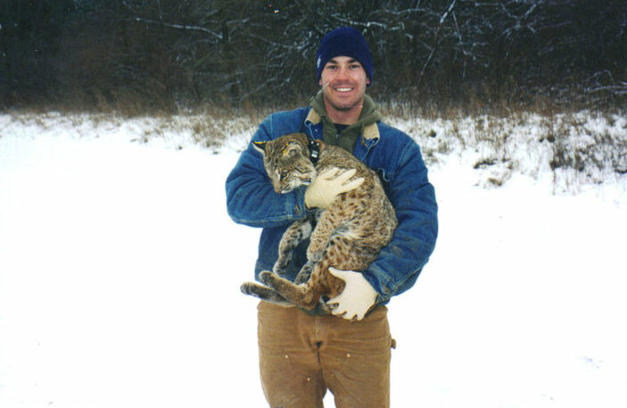 Calvin Duncan holding a sedated bobcat while working on a research project in Iowa.